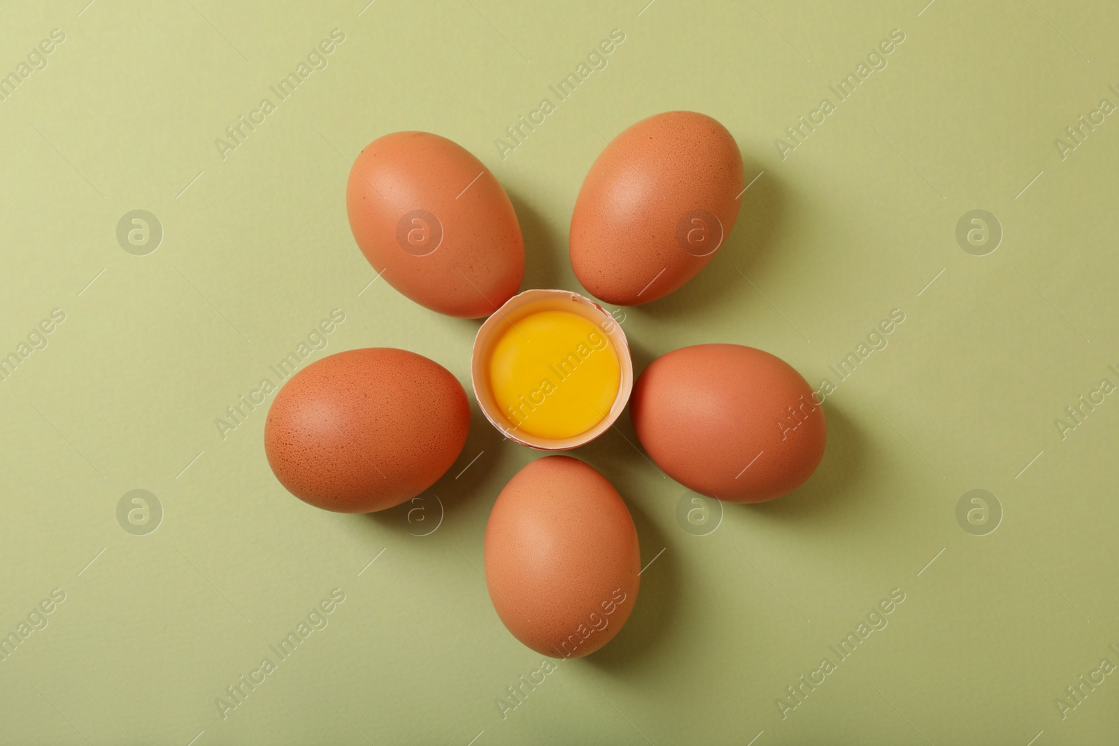 Photo of Flower made with cracked and whole chicken eggs on olive background, flat lay