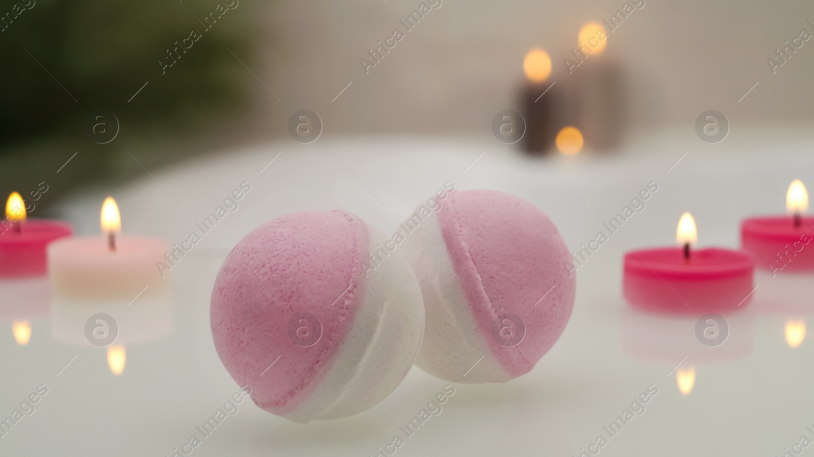 Photo of Bath bombs with burning candles on tub indoors, closeup. Bokeh effect