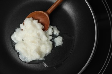 Photo of Frying pan with coconut oil and wooden spatula, top view. Healthy cooking