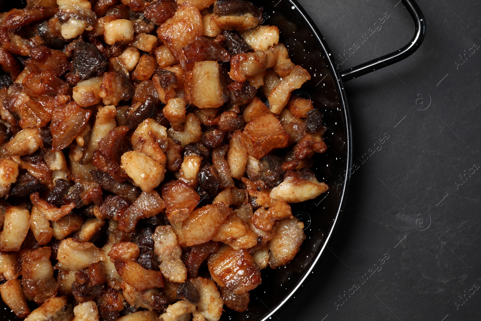 Photo of Tasty fried cracklings on black table, top view. Cooked pork lard