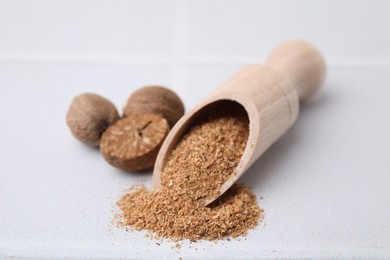 Photo of Scoop with grated nutmeg and seeds on white table, closeup