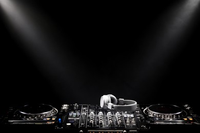 Photo of Modern DJ controller and headphones under beams of light on black background