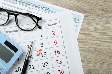 Tax day. Calendar with date reminder, document, glasses, pen and calculator on wooden table, flat lay. Space for text