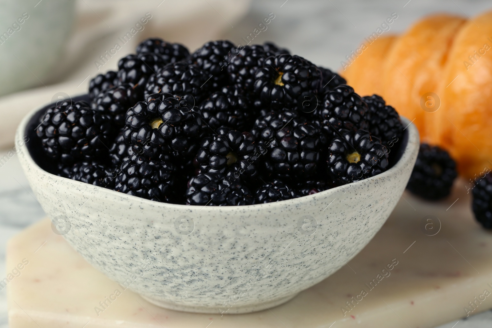 Photo of Bowl of fresh ripe blackberries on white marble table, closeup