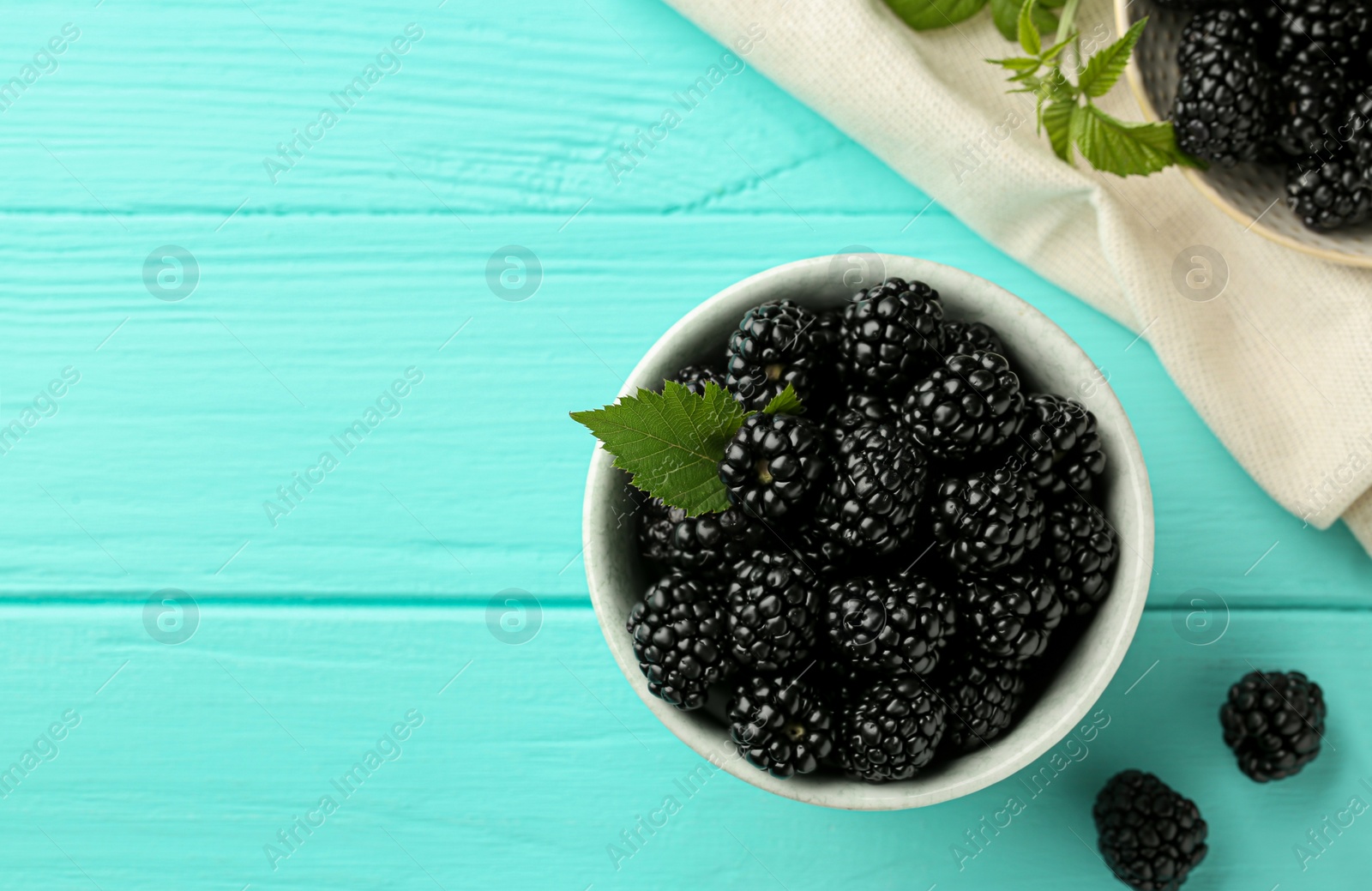 Photo of Bowl of fresh ripe blackberries on turquoise wooden table, flat lay. Space for text