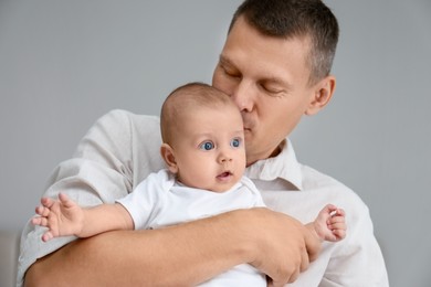 Father holding his cute baby on grey background