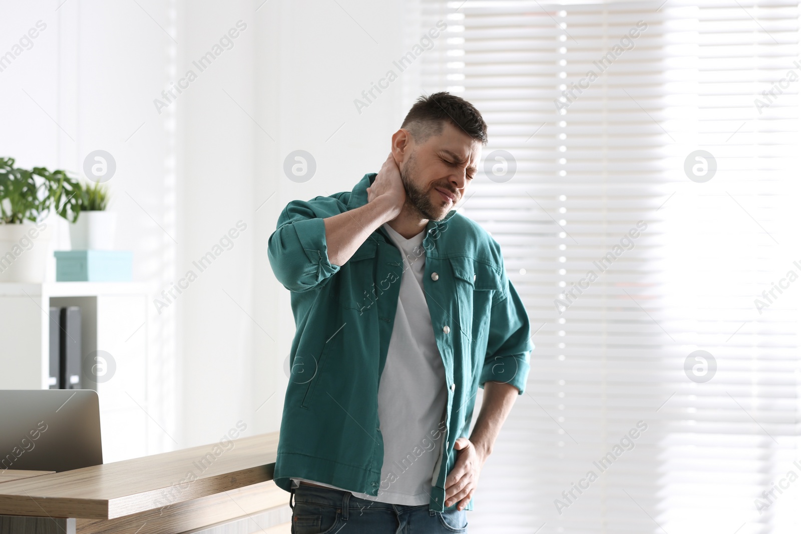 Photo of Man suffering from neck pain in office. Bad posture problem