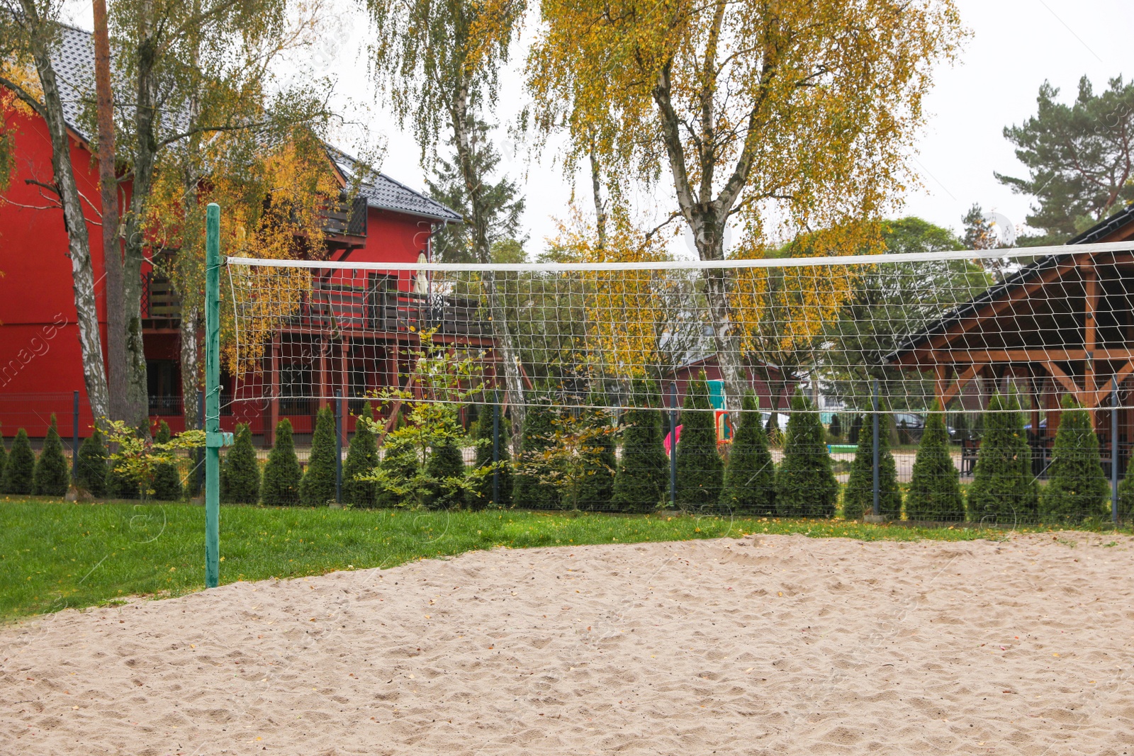 Photo of Sand volleyball court with net near trees and buildings