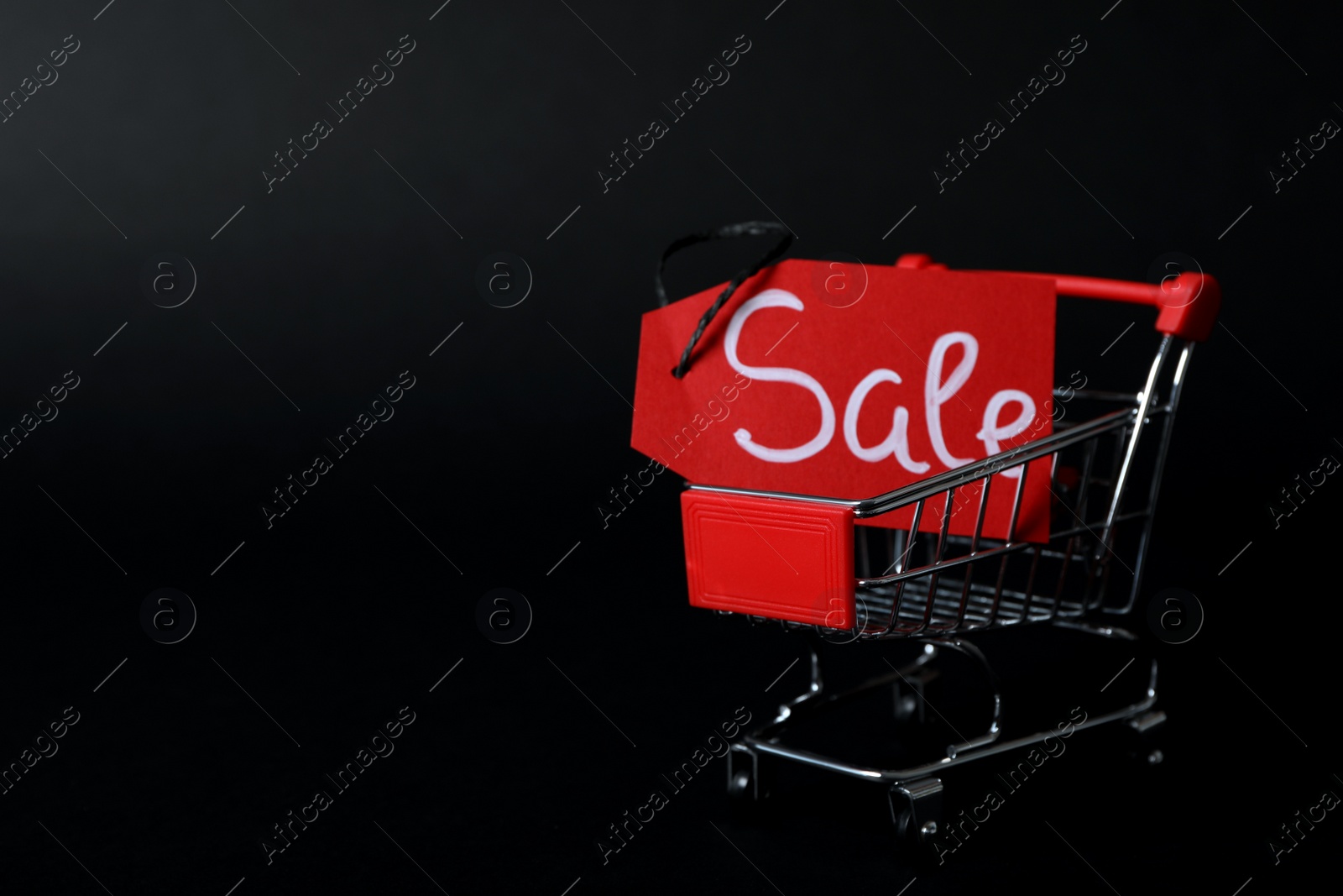 Photo of Tag with word Sale and toy shopping cart on dark background, space for text. Black friday concept