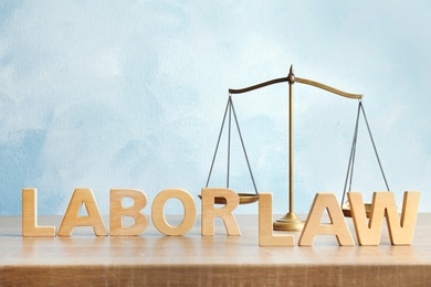 Words LABOR LAW and scales of justice on table against color background