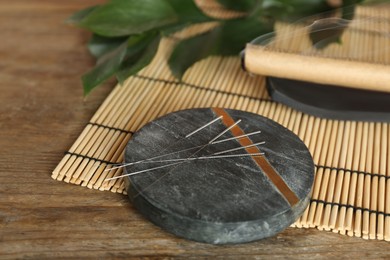 Grey stone coaster with acupuncture needles on wooden table