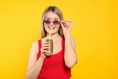 Beautiful happy woman drinking from beverage can on yellow background. Space for text