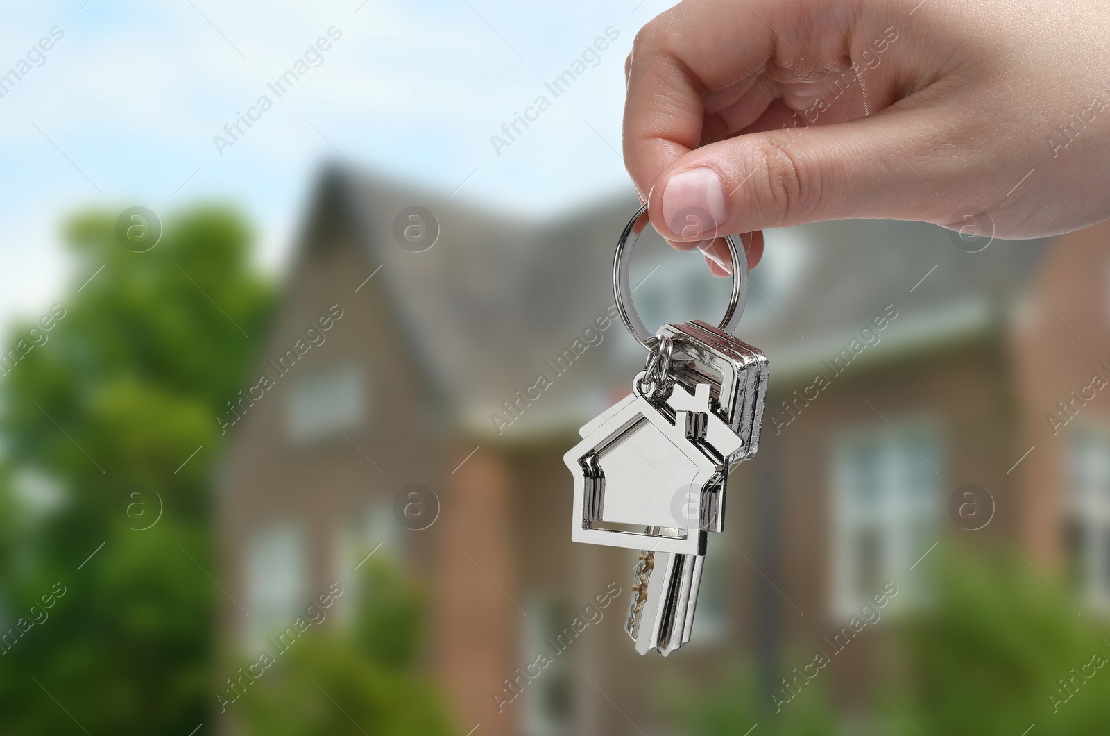 Image of Woman holding keys near house outdoors, closeup