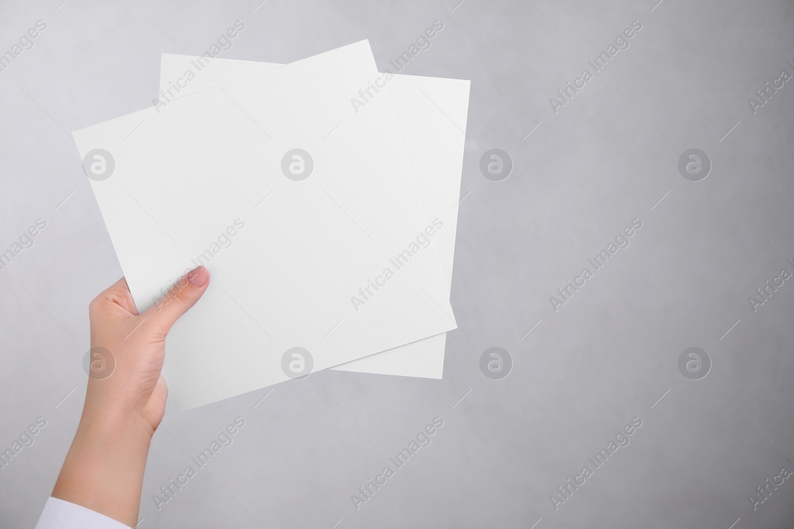 Photo of Young woman holding blank paper sheets on light grey background, closeup. Mock up for design