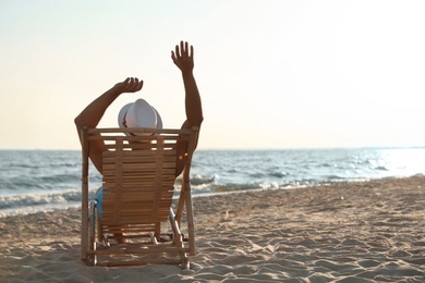 Photo of Young man relaxing in deck chair on beach near sea