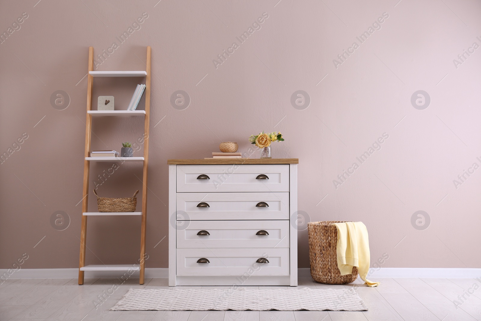 Photo of Elegant room interior with stylish chest of drawers, shelving unit and wicker basket