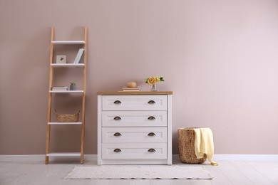 Elegant room interior with stylish chest of drawers, shelving unit and wicker basket