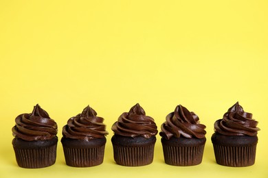 Photo of Delicious chocolate cupcakes with cream on yellow background. Space for text