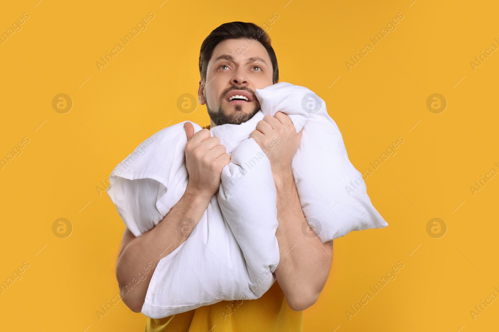 Photo of Tired man with pillow on yellow background. Insomnia problem