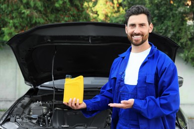 Smiling worker showing yellow container of motor oil near car outdoors