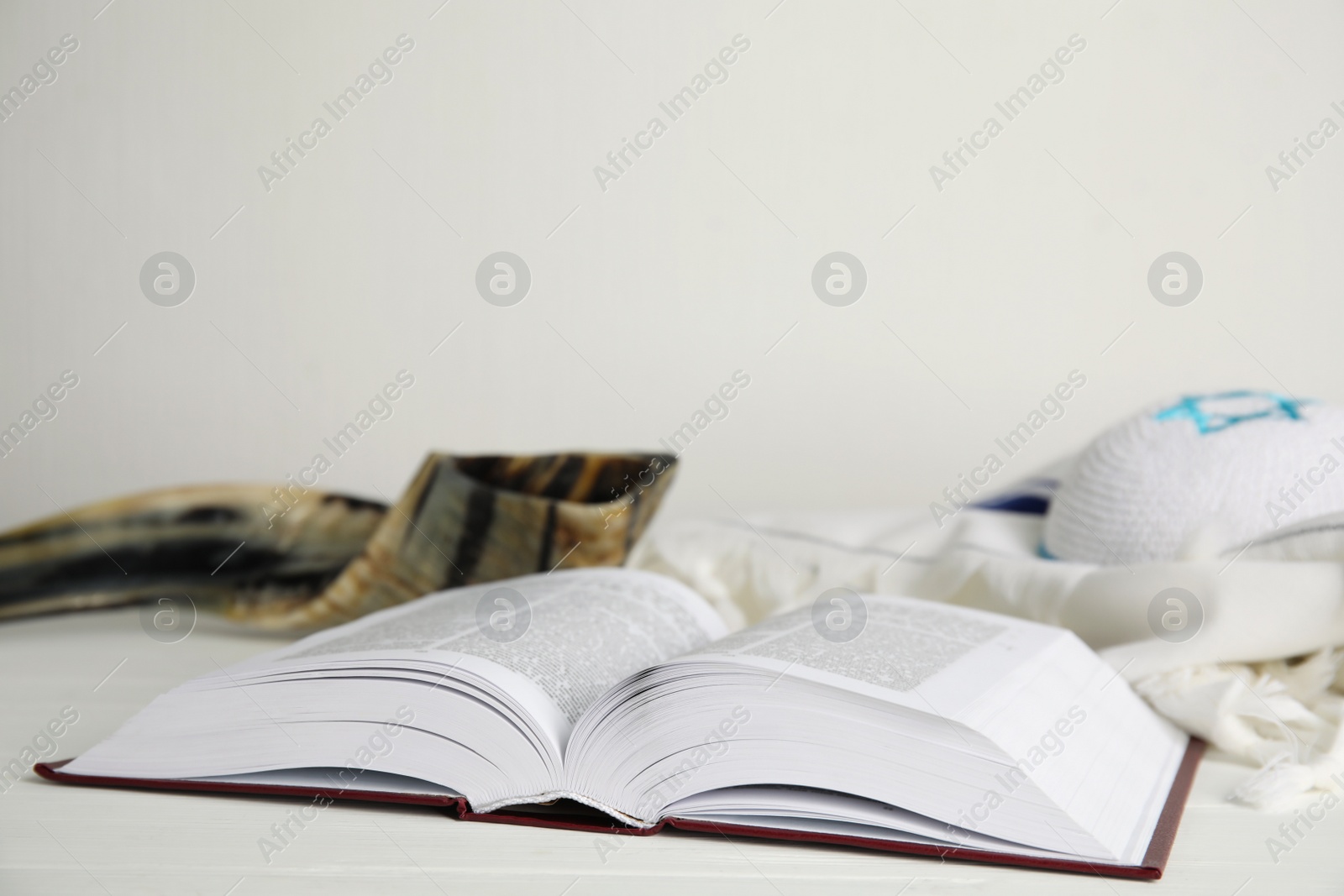 Photo of Open Torah, shofar and tallit on white wooden table, space for text. Rosh Hashanah celebration