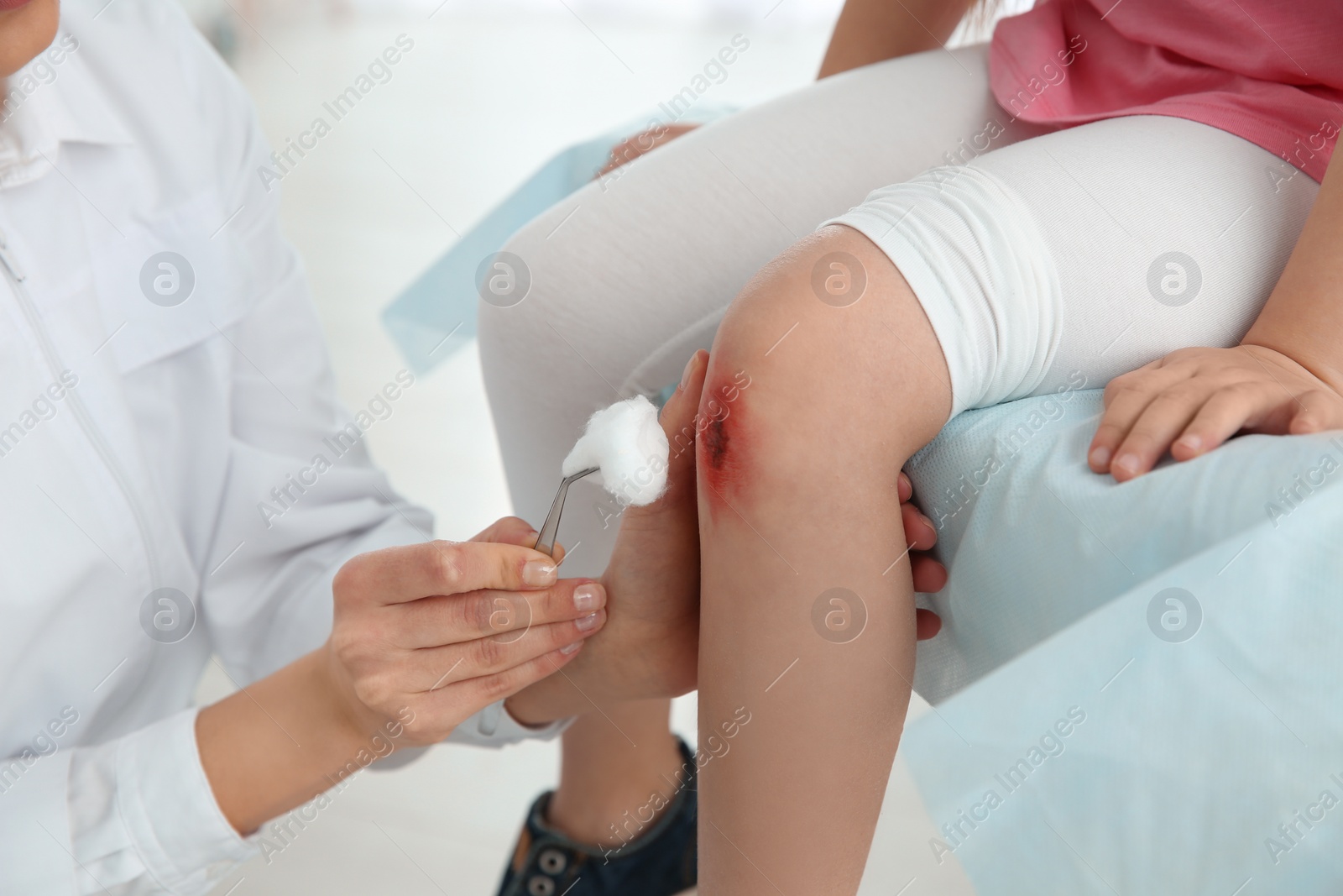 Photo of Female doctor cleaning little girl's leg injury in clinic, closeup. First aid