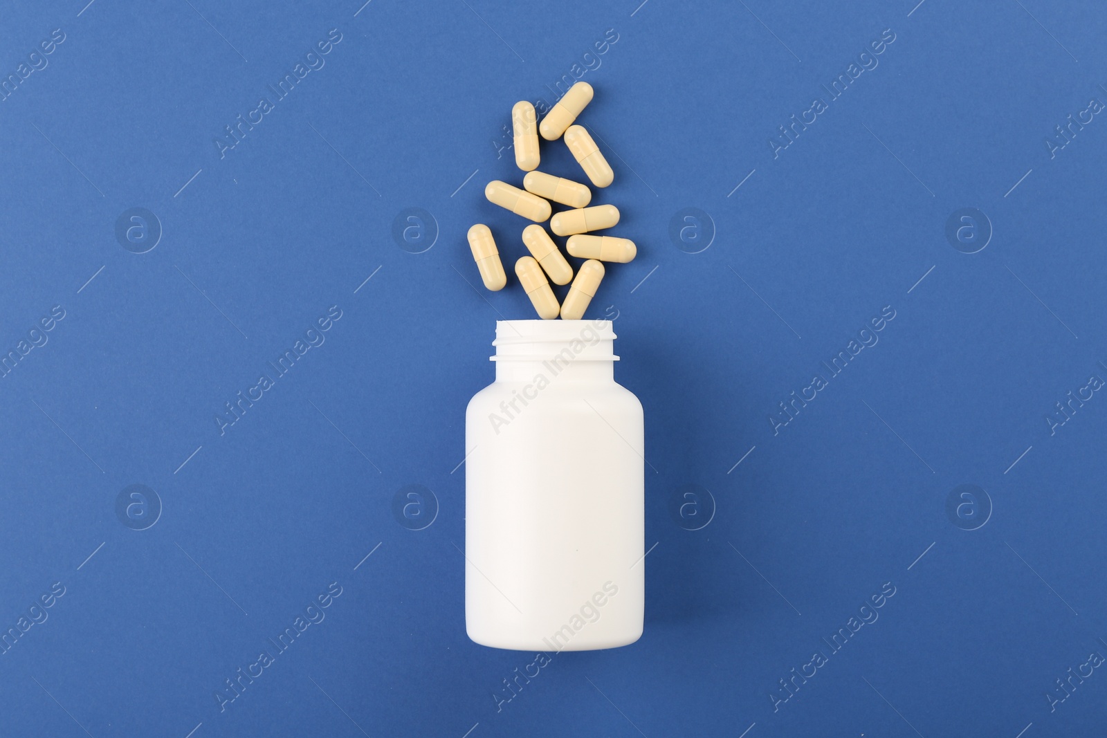 Photo of Bottle and vitamin capsules on blue background, top view