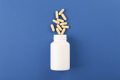 Bottle and vitamin capsules on blue background, top view