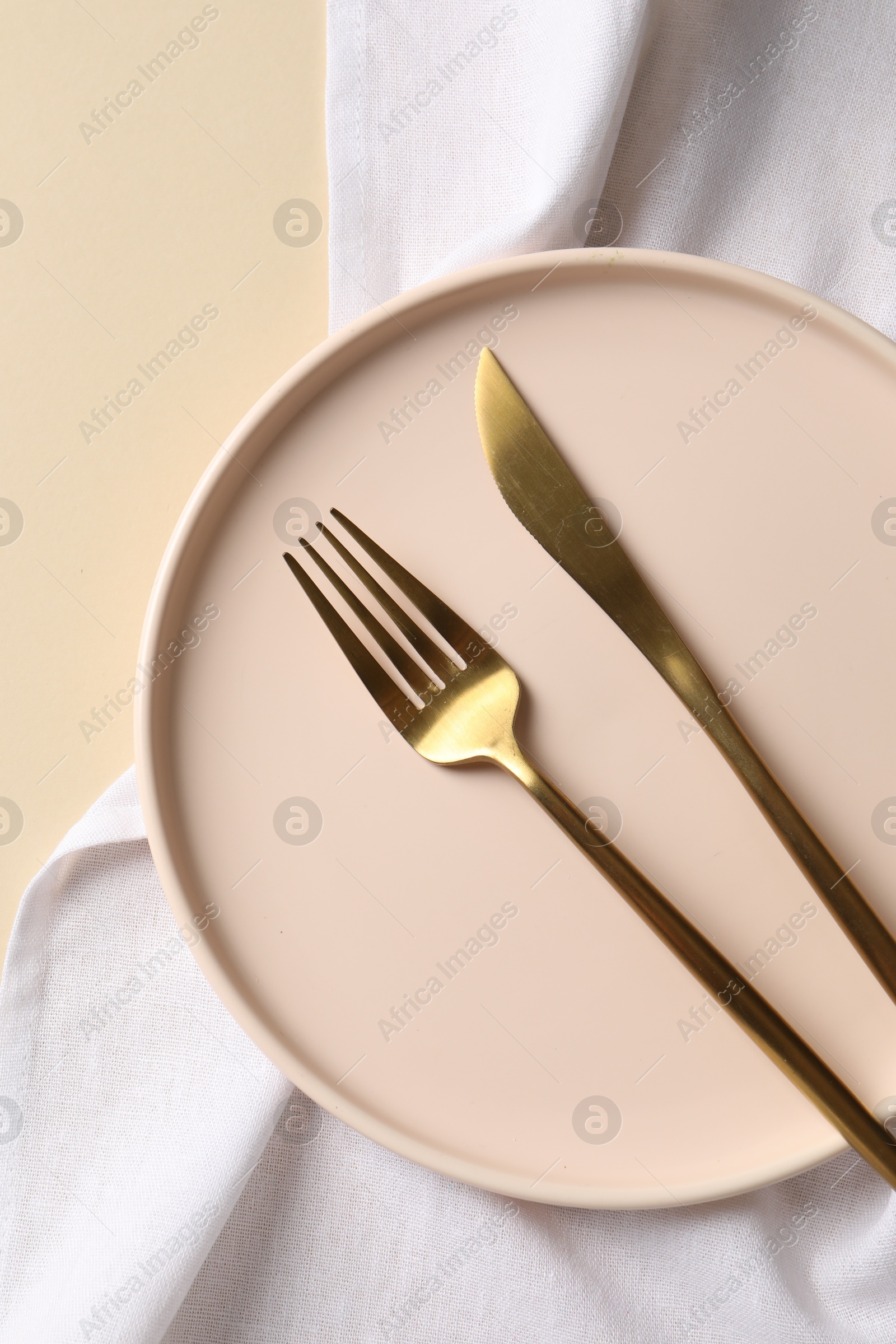 Photo of Stylish golden cutlery, plate and napkin on beige background, top view