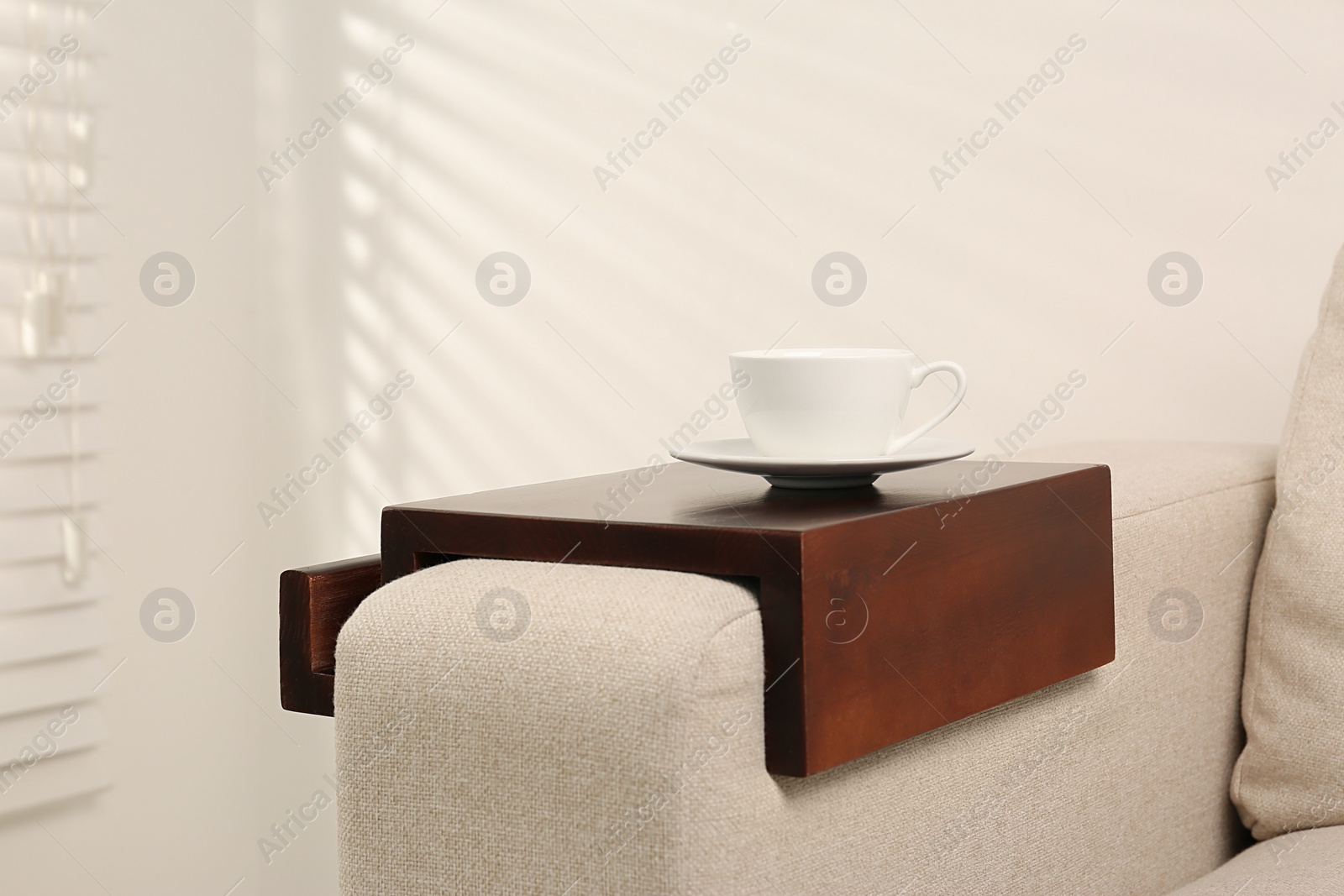 Photo of Cup of coffee on sofa with wooden armrest table indoors. Interior element