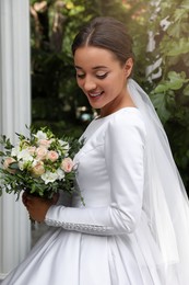 Young bride wearing wedding dress with beautiful bouquet in park