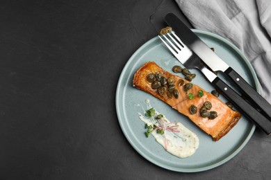 Photo of Delicious salmon with capers and sauce served on dark table, top view. Space for text