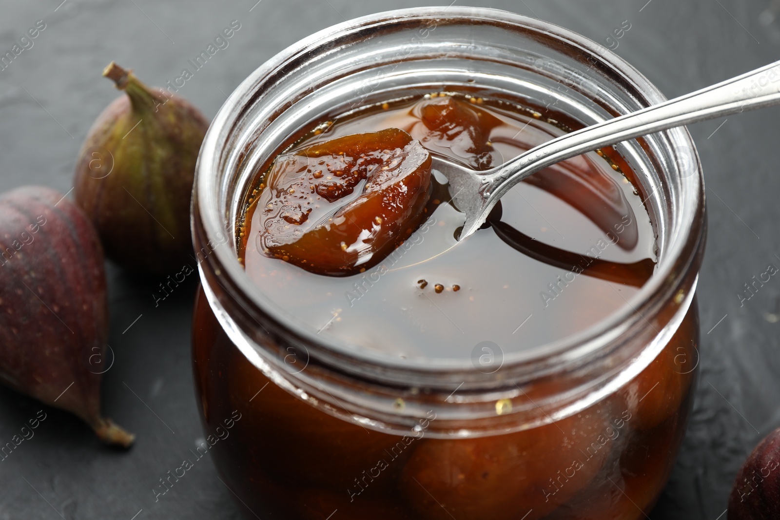 Photo of Jar of tasty sweet jam and fresh figs on black table, closeup