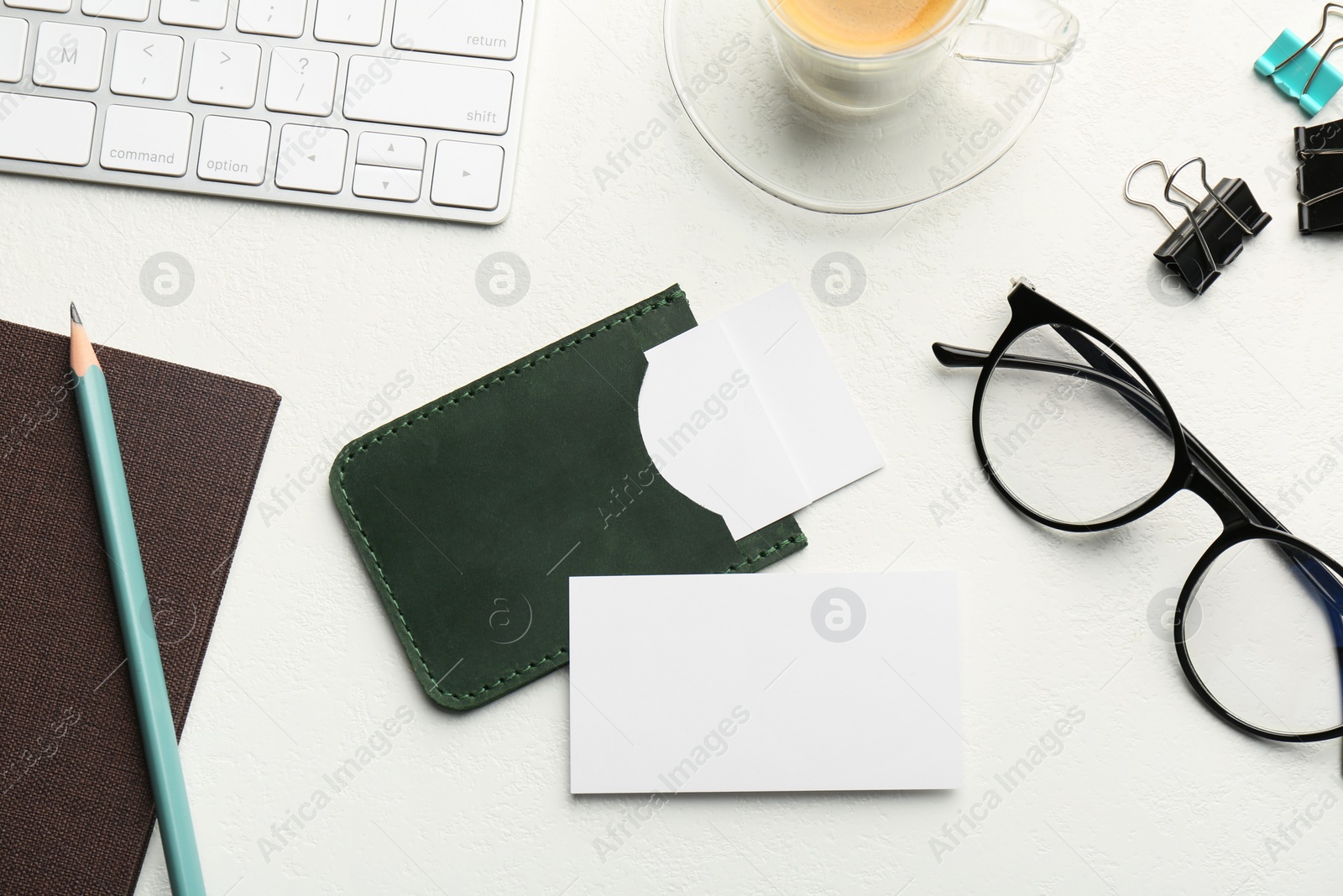 Photo of Leather business card holder with blank cards, glasses, keyboard and stationery on white table, flat lay
