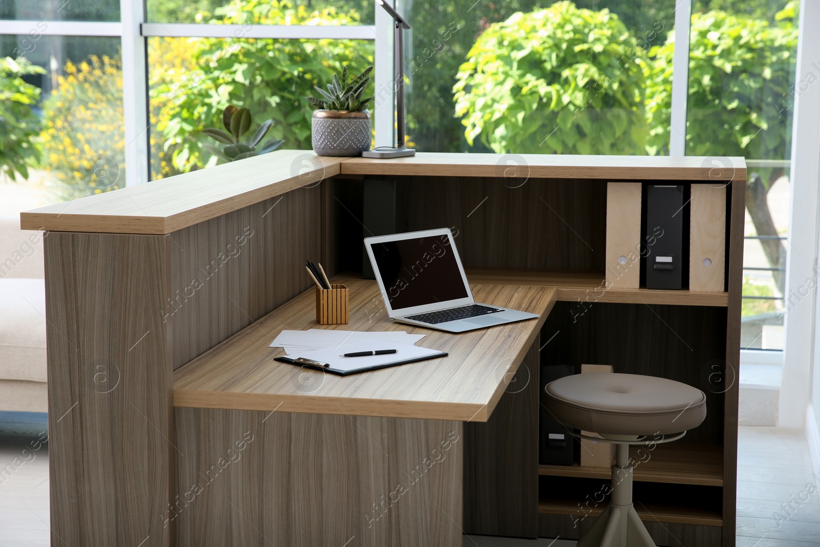 Photo of Stylish modern wooden desk with laptop indoors. Receptionist workplace