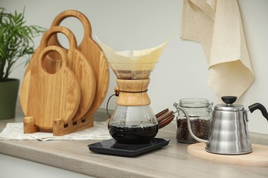 Making drip coffee. Glass chemex coffeemaker with paper filter, jar of beans and kettle on wooden countertop in kitchen