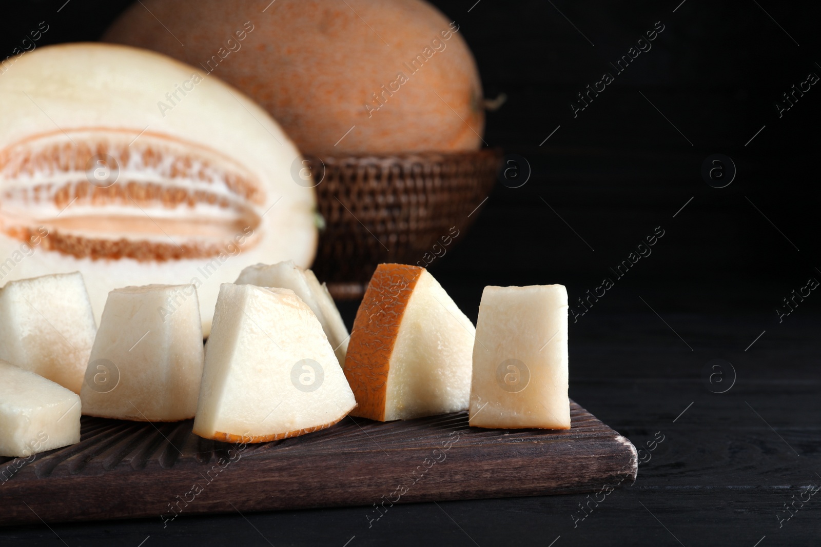Photo of Pieces of delicious honey melon on black wooden table, closeup