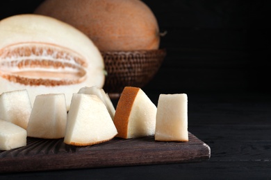 Photo of Pieces of delicious honey melon on black wooden table, closeup