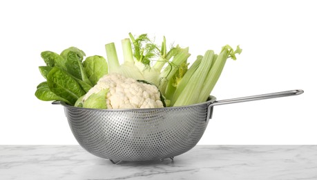 Photo of Metal colander with different vegetables on marble table against white background