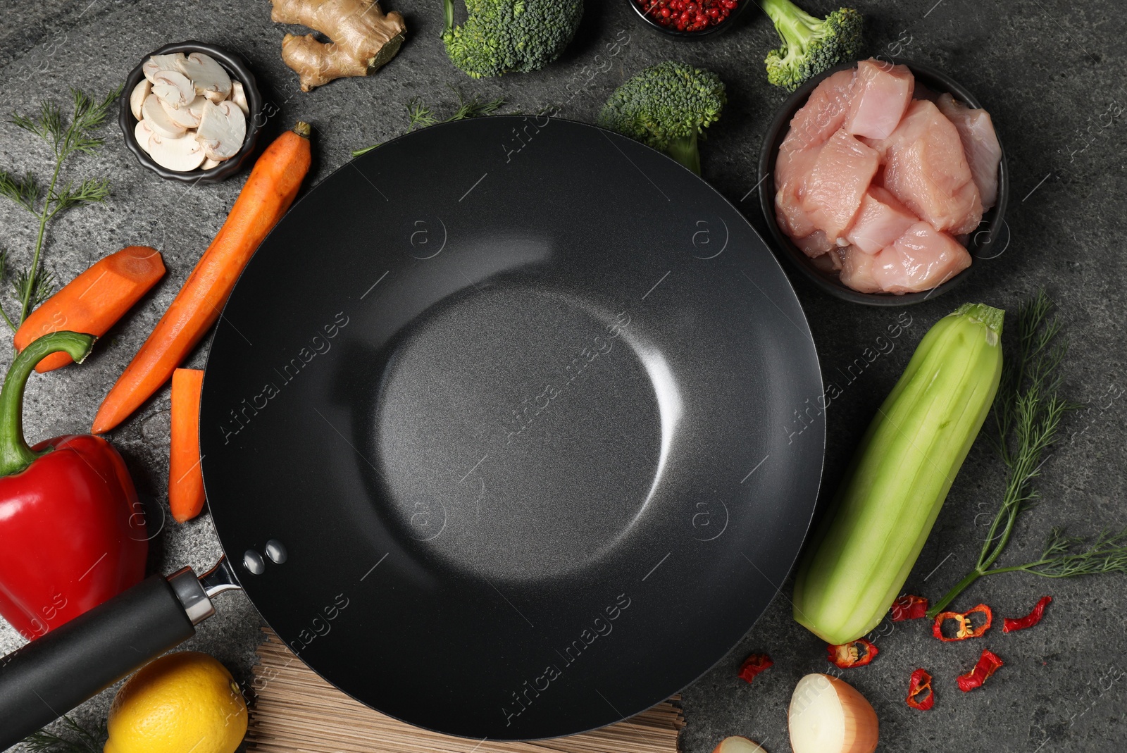 Photo of Empty iron wok surrounded by raw ingredients on grey table, flat lay