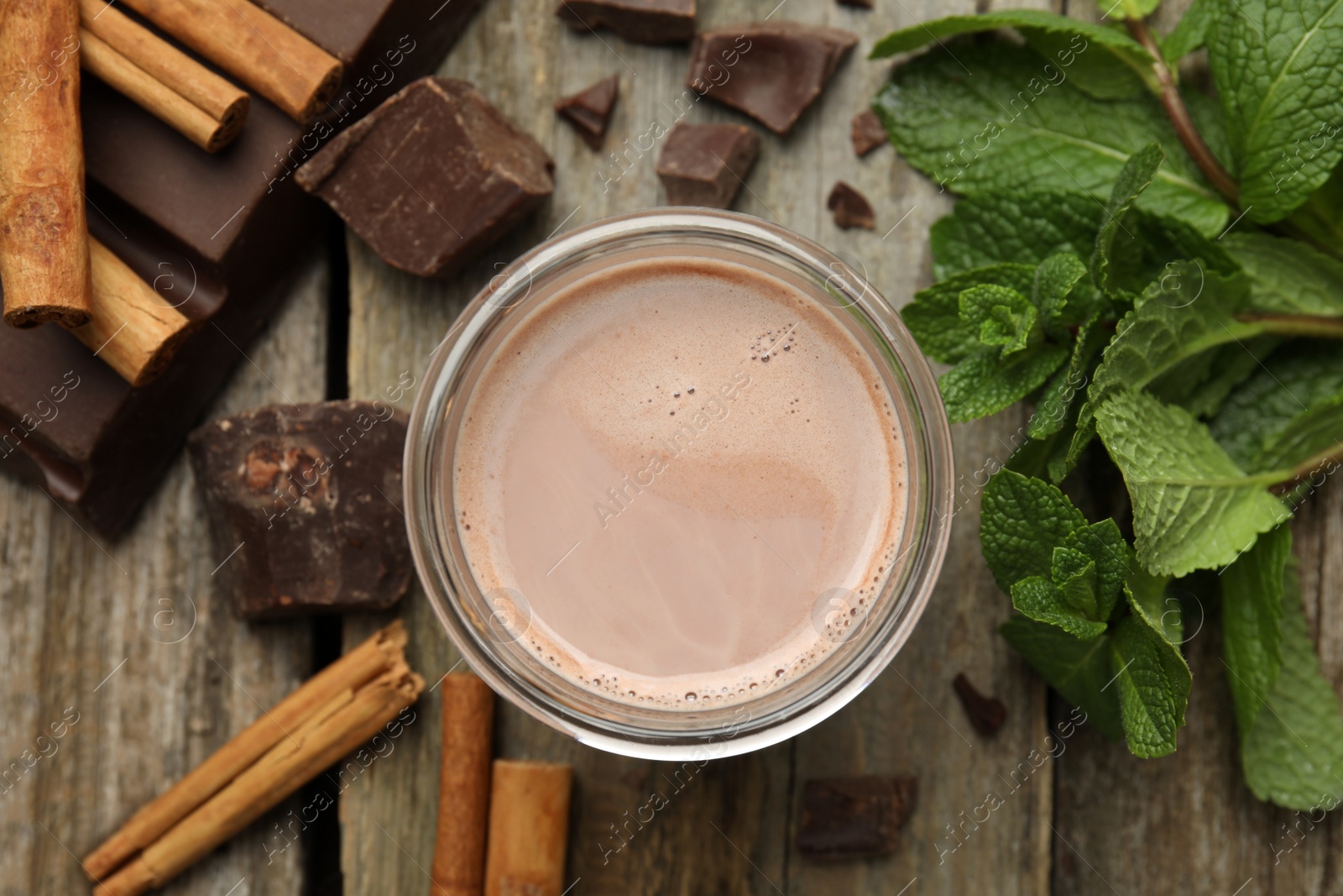 Photo of Glass of delicious hot cocoa with chunks, fresh mint and cinnamon sticks on wooden table, flat lay