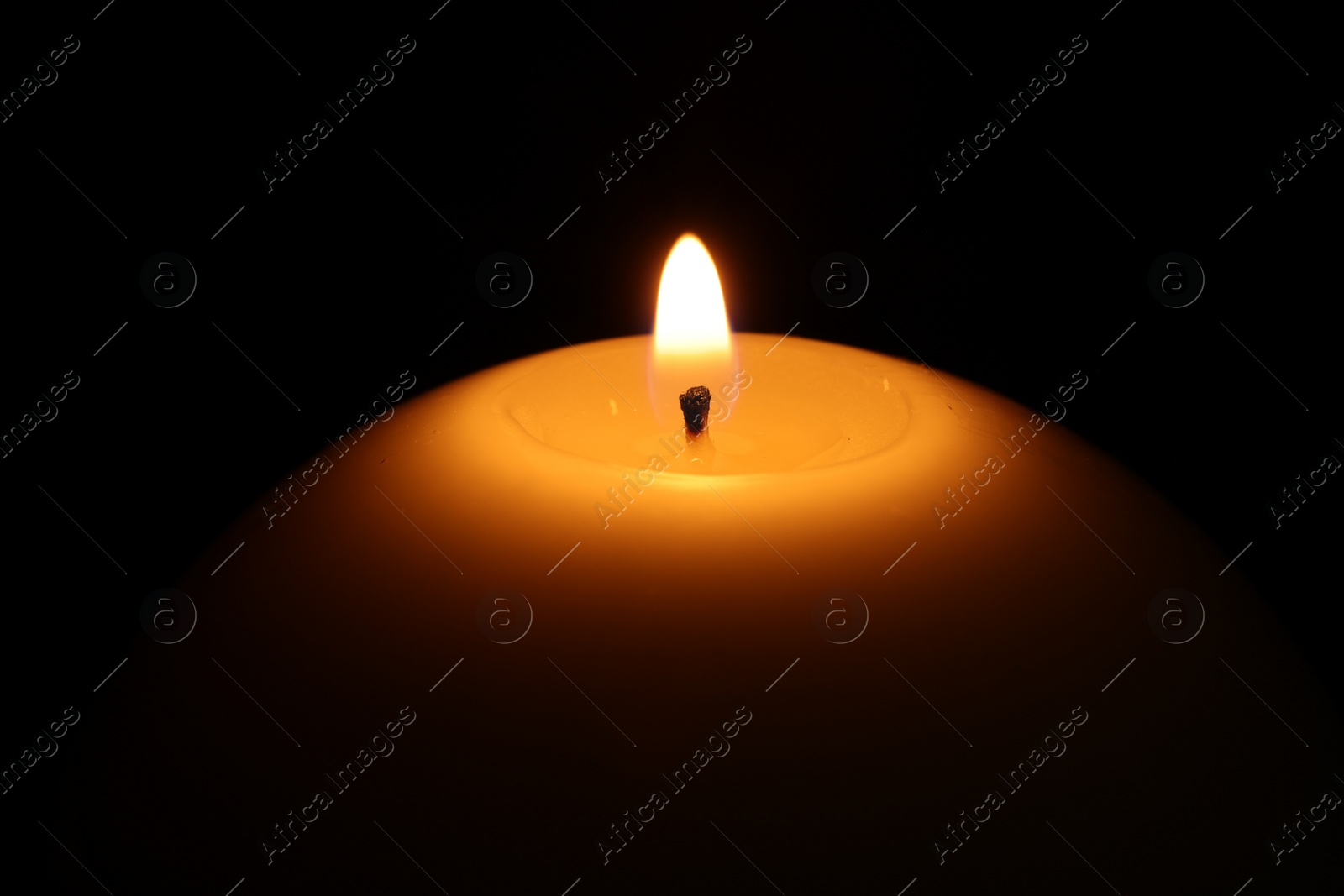 Photo of Burning wax candle on black background, closeup