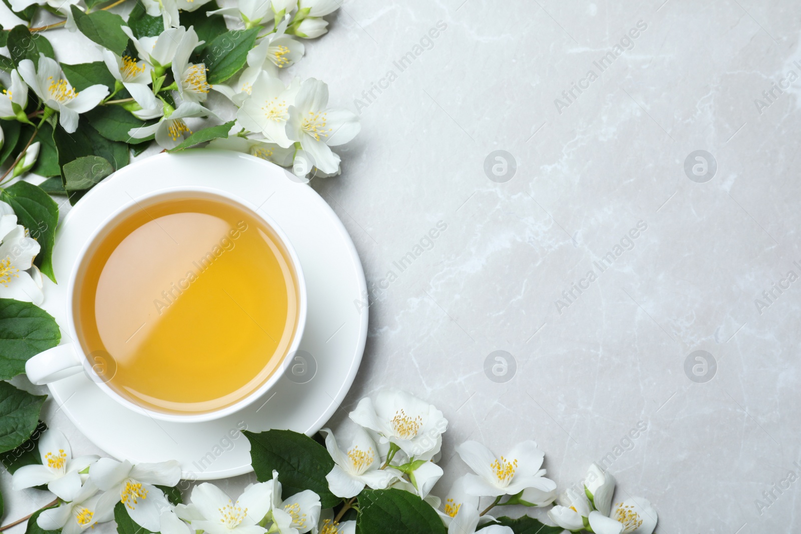 Photo of Cup of tea and fresh jasmine flowers on light grey marble table, flat lay. Space for text