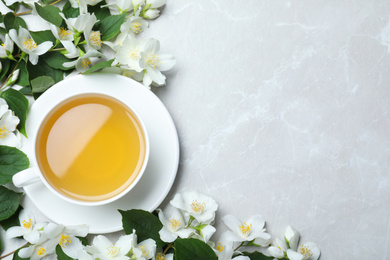 Cup of tea and fresh jasmine flowers on light grey marble table, flat lay. Space for text