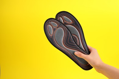 Photo of Woman holding pair of orthopedic insoles on yellow background, closeup. Space for text
