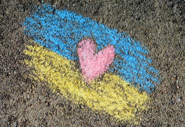 Photo of National flag of Ukraine with heart drawn by color chalk on asphalt, top view