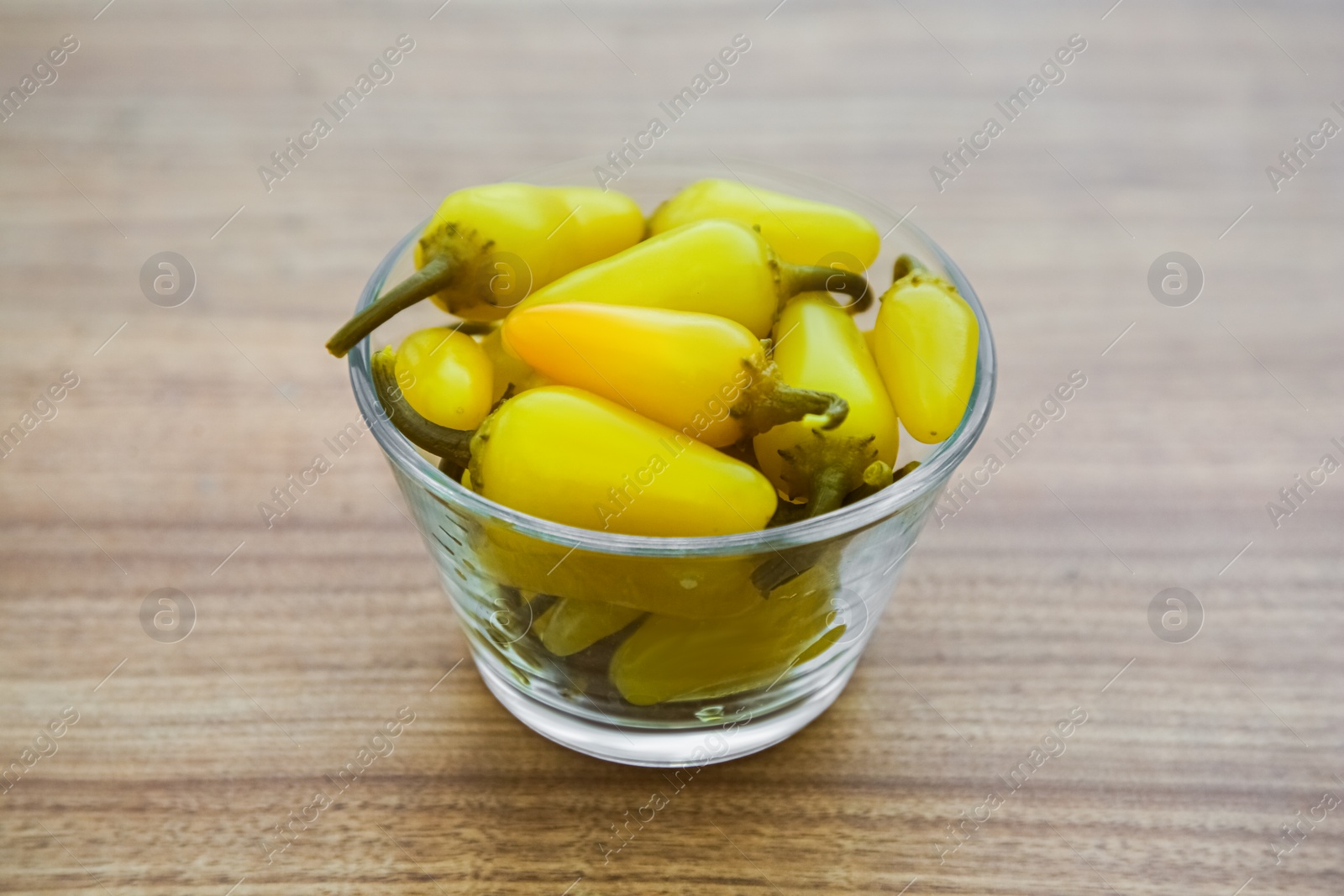 Photo of Glass bowl of pickled yellow jalapeno peppers on wooden table, closeup