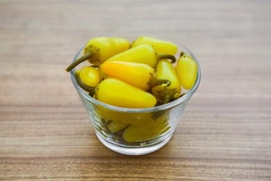 Photo of Glass bowl of pickled yellow jalapeno peppers on wooden table, closeup