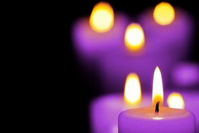 Burning violet candle on black background, closeup. Funeral attributes