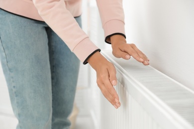 Photo of Woman warming hands on heating radiator near white wall, closeup